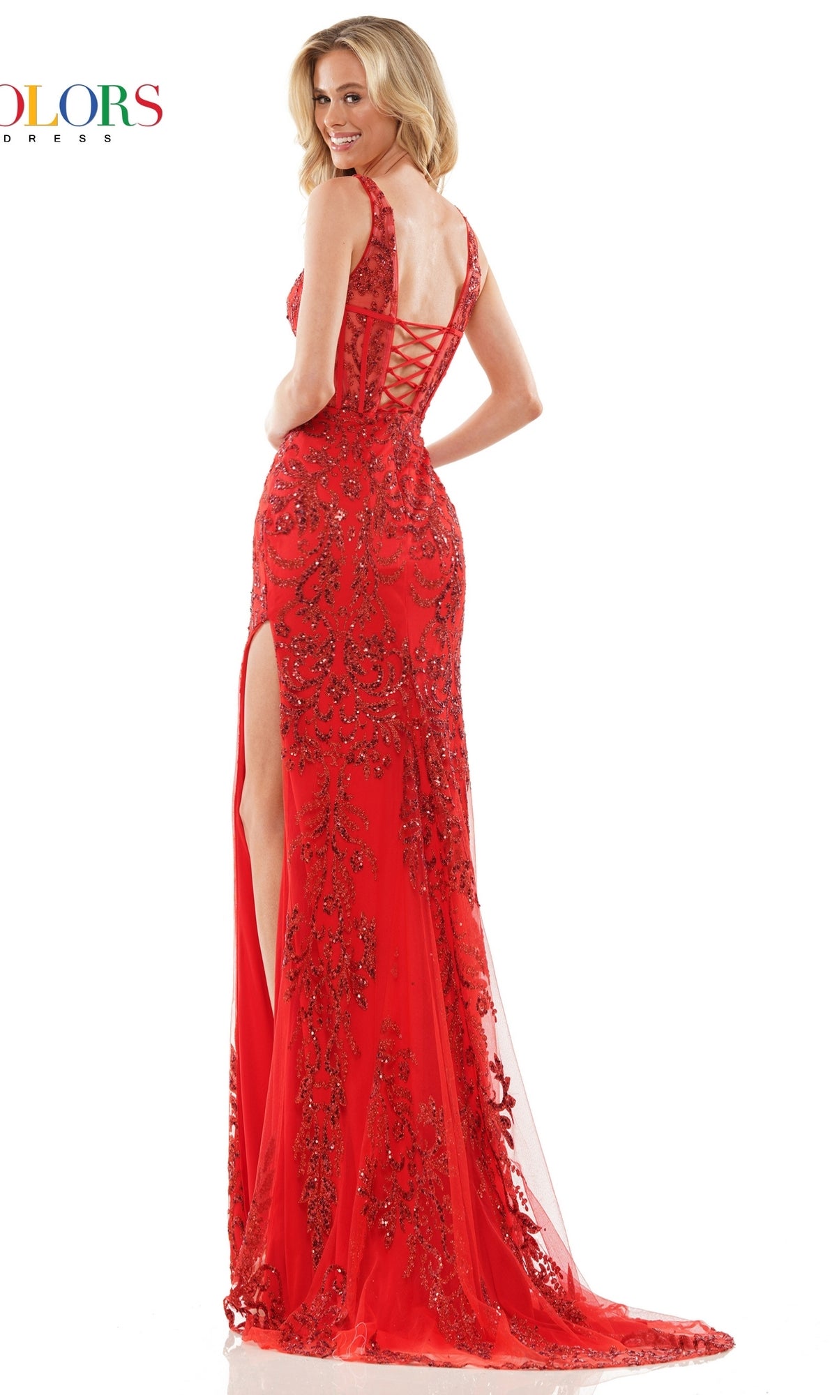 A woman in the Sheer-Waist Glitter-Print Long Prom Dress 2990—a red, floor-length gown with a lace-up back, high slit, and intricate glitter pattern—stands posed with a smile.